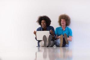 casal multiétnico sentado no chão com um laptop e tablet foto