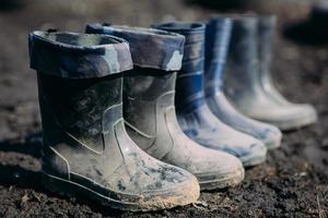 variedade de botas de borracha em uma linha na sujeira no início da primavera foto