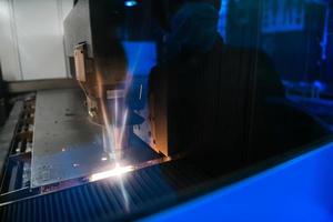 faíscas voam para fora da cabeça da máquina para metal a laser de processamento de metal no fundo da planta metalúrgica. fabricação de peças acabadas para o conceito de produção automotiva foto