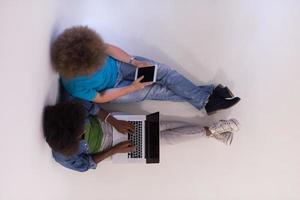 casal multiétnico sentado no chão com um laptop e tablet vista superior foto