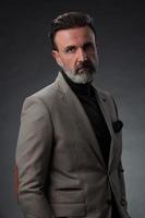 retrato de um elegante elegante empresário sênior com barba e roupas de negócios casuais em estúdio fotográfico isolado em fundo escuro, gesticulando com as mãos foto
