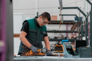 interior da fábrica de engenharia da indústria pesada com trabalhador industrial usando rebarbadora e cortando um tubo de metal. empreiteiro em uniformes de segurança e fabricação de capacetes de estruturas metálicas. foto