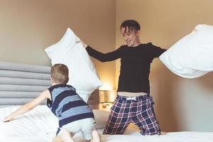feliz pai e filho se divertindo enquanto luta de travesseiros no quarto. foto