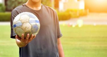 um velho futebol segurando na mão do jogador, foco suave e seletivo no futebol, fundo editado pela luz do sol. foto