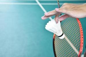 jogador de badminton segura raquete e peteca de creme branco na frente da rede antes de servir para o outro lado da quadra. foto