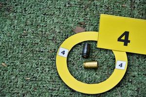 cartuchos de bala de pistola e sinal de papel amarelo no chão, conceito para manter evidências físicas do uso de pistolas, armas e cartuchos de bala no ponto do assassinato. foto