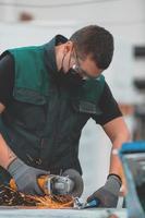 interior da fábrica de engenharia da indústria pesada com trabalhador industrial usando rebarbadora e cortando um tubo de metal. empreiteiro em uniformes de segurança e fabricação de capacetes de estruturas metálicas. foto