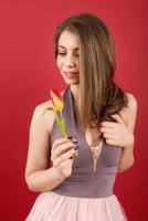 adolescente posando com tulipa em mãos sobre fundo vermelho foto