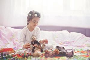 menina bonitinha, brincando com bonecas na cama em casa foto