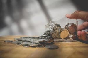 mão de homem colocando copo de moedas na mesa de madeira foto