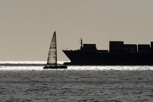 barco a vela e grande silhueta de navio porta-contentores foto