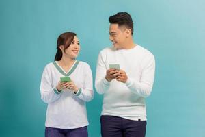 alegre casal jovem isolado sobre fundo azul, segurando telefones inteligentes em roupas casuais foto