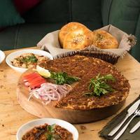 um close-up de um lahmacun e uma salada perto da cesta de pães
