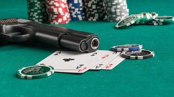 um close-up de uma arma ao lado de algumas cartas de baralho e fichas de pôquer em um tabuleiro verde. foto