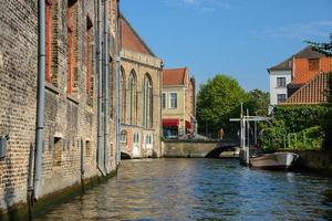 vista do canal para a ponte, barco e antigas casas de mercadores de tijolos em bruges, bélgica. antiga vista da cidade da europa medieval. foto
