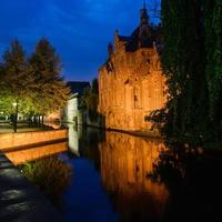 antiga casa de tijolos medievais na europa refletida na água dos canais vista em bruges, bélgica. cena noturna com iluminação e reflexos foto