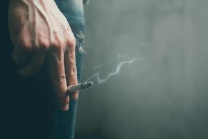 homem segurando um cigarro na mão. a fumaça do cigarro se espalha. fundo escuro foto