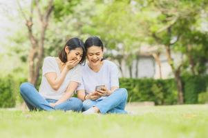 mulheres asiáticas rindo enquanto estiver usando o smartphone ao ar livre foto