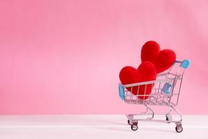 formas de coração vermelho no carrinho de compras em fundo rosa foto