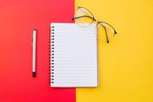 caderno, óculos e caneta em fundo vermelho e amarelo foto