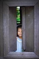 jovem menina asiática picos através da janela na câmera foto