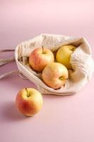 maçãs na sacola de compras reutilizáveis em fundo rosa foto