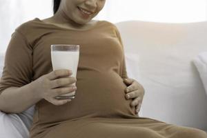 mulher grávida asiática senta-se com copo de leite foto