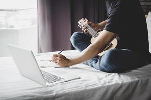 jovem na cama toca música com guitarra foto