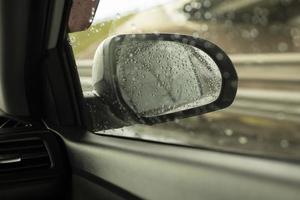 espelho retrovisor do carro atrás do vidro molhado. vista da estrada na chuva. detalhes da viagem. foto