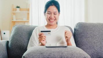 mulher asiática usando tablet e cartão de crédito na sala de estar. foto