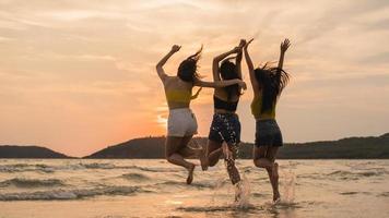 grupo de três jovens mulheres asiáticas pulando na praia.
