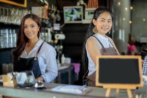 baristas asiáticos femininos sorrindo atrás do balcão da loja de café foto