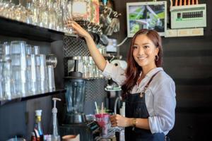 barista asiático feminino, sorrindo enquanto estiver usando a máquina de café foto