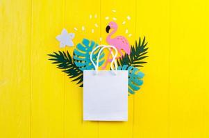 maquete de papel em branco com folhas e flamingo em fundo amarelo de madeira foto