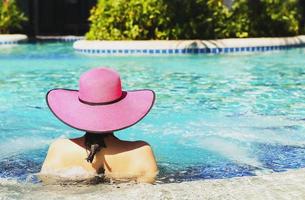 mulher de chapéu rosa relaxante na piscina foto