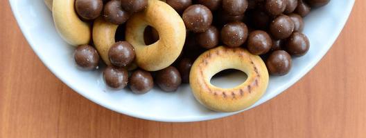 túbulos crocantes, bolas de chocolate derretendo e bagels estão em um prato branco sobre uma mesa de madeira. mistura de vários doces foto