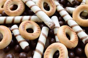 muitos túbulos doces crocantes, bolas de chocolate derretidas e bagels amarelos estão em uma superfície de madeira. vista de perto foto