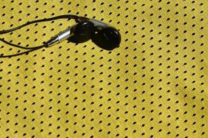 fones de ouvido pretos repousam sobre a roupa esportiva amarela de fibra de nylon de poliéster. o conceito de ouvir música durante o treinamento esportivo com tecnologia moderna foto