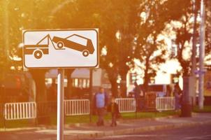 um sinal de estrada que mostra um caminhão de reboque de carro, que levanta um carro de passeio a bordo foto