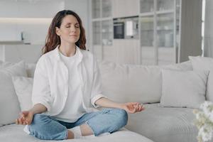 feminina pratica ioga senta-se no sofá em pose de lótus. hábitos saudáveis, estilo de vida consciente, alívio da ansiedade foto