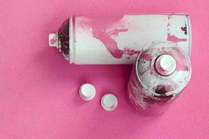 algumas latas de spray de aerossol rosa usadas e bicos com gotas de tinta ficam em um cobertor de tecido de lã rosa claro macio e peludo. cor de design feminino clássico. conceito de vandalismo de graffiti foto