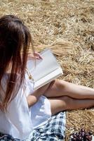 jovem de vestido branco sentado no palheiro no campo colhido, lendo o livro em branco. maquete de livro foto