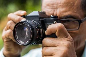 close-up de um homem idoso tirando fotos com uma câmera de filme antigo.