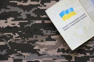 sumy, ucrânia - 20 de março de 2022 passaporte estrangeiro ucraniano em tecido com textura de camuflagem militar pixelizada. pano com padrão de camuflagem em formas de pixel cinza, marrom e verde e identificação ucraniana foto