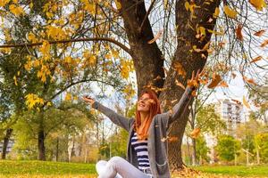 mulher lúdica jogando folhas no ar eu parque outono. foto