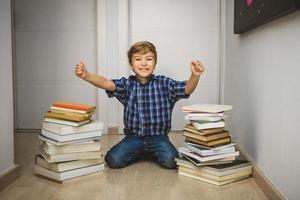 garoto animado com as mãos levantadas com livros ao seu redor. foto