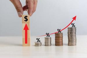 negócios finanças investimentos economia pilha moeda inflação e seta vermelha com porcentagem de cubo de madeira na mesa. foto