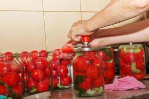 o processo de conservação de tomates para o inverno. as mãos das mulheres fecham as tampas dos frascos com tomates suculentos vermelhos maduros com uma chave especial. foto