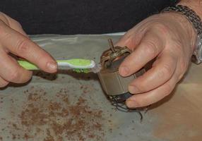 limpar um exaustor de cozinha muito sujo da sujeira com uma escova. um homem limpa as partes de um ventilador com uma escova foto