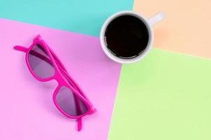 xícara de café branca pequena e óculos de sol rosa no fundo das cores pastel de moda rosa, azul, coral e limão foto